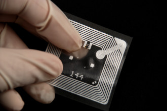 A Hand on blck background which holds a RFID Tag
