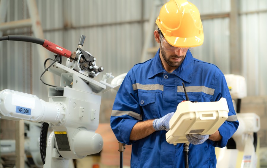 A human holding a console in his hand. A robot arm can be seen in the background