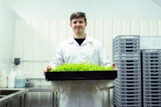 Photo of a Person in laboratory coat holding plants in a plastic container