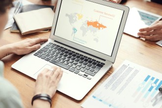 Image of a Person sitting infront of a Laptop and Looking at a Worldmap with Matrics for Business