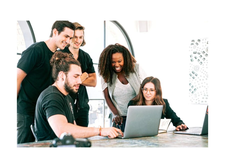 Image of a group of people where two of them sit and three of them stand infront of a laptop.