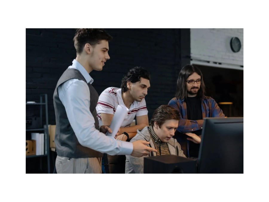 Image of Four People surrounding a Computer and Talking about Something