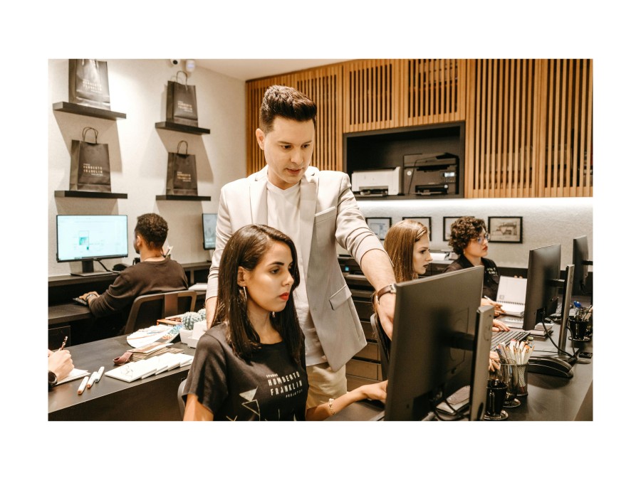 Picture of a Man and a Woman infront of a Computer, where the Man in a Suit is showing the Woman something on the Display