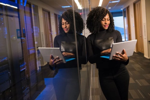 Picture of a Woman in a Black Shirt with a Laptop in front of a Server behind a Glass Wall