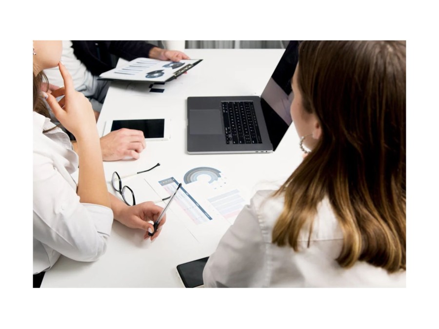 Picture of three People sitting around a Table, that has several Documents with different Graphs and a Laptop on it