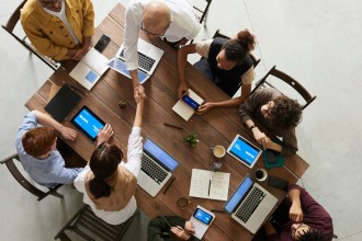 Image of Several People Sitting Around a Table and Infront of their Laptops, while Two of Them are Shaking Hands