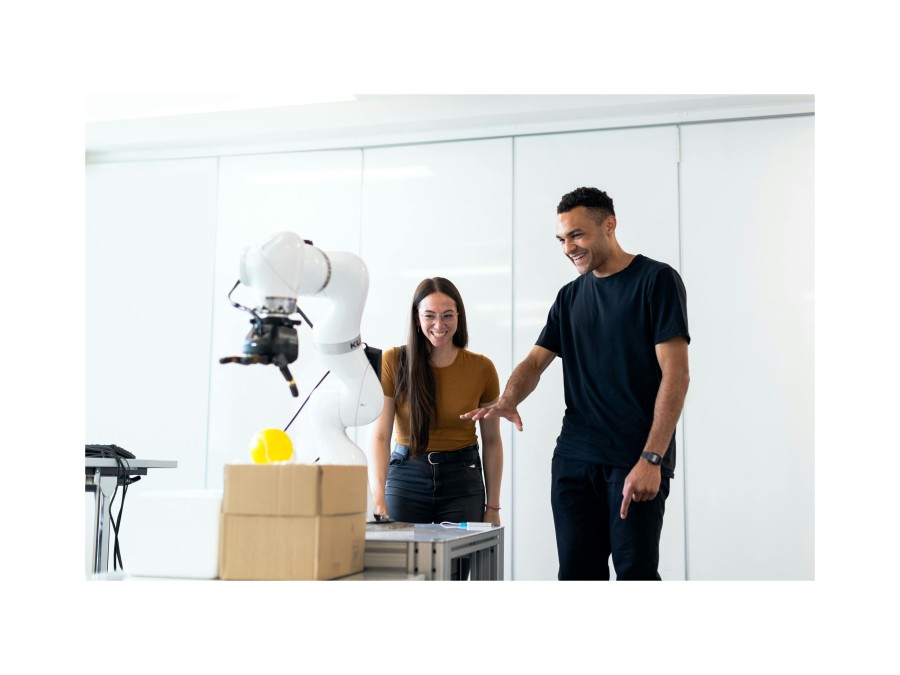 Photo of a Man and a Woman Standing behind a White Robot Arm